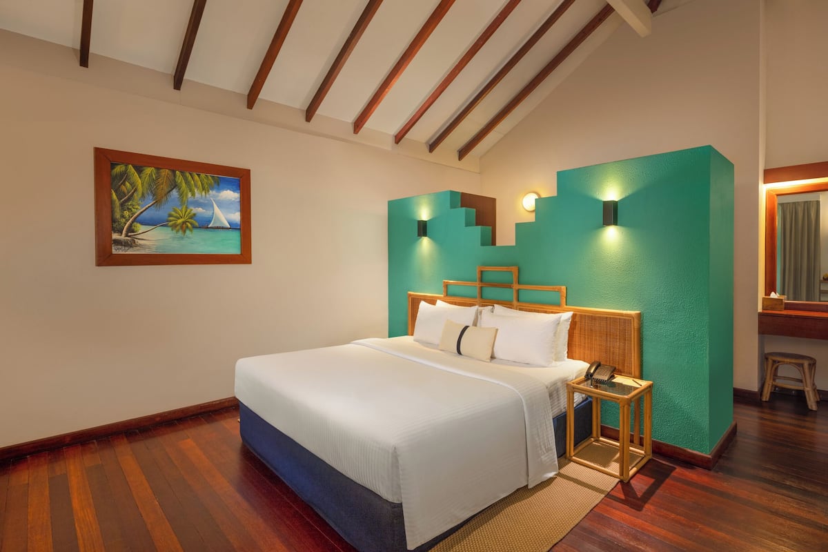 A bedroom with a bed, wooden headboard, nightstands, a painting, and a teal accent wall.