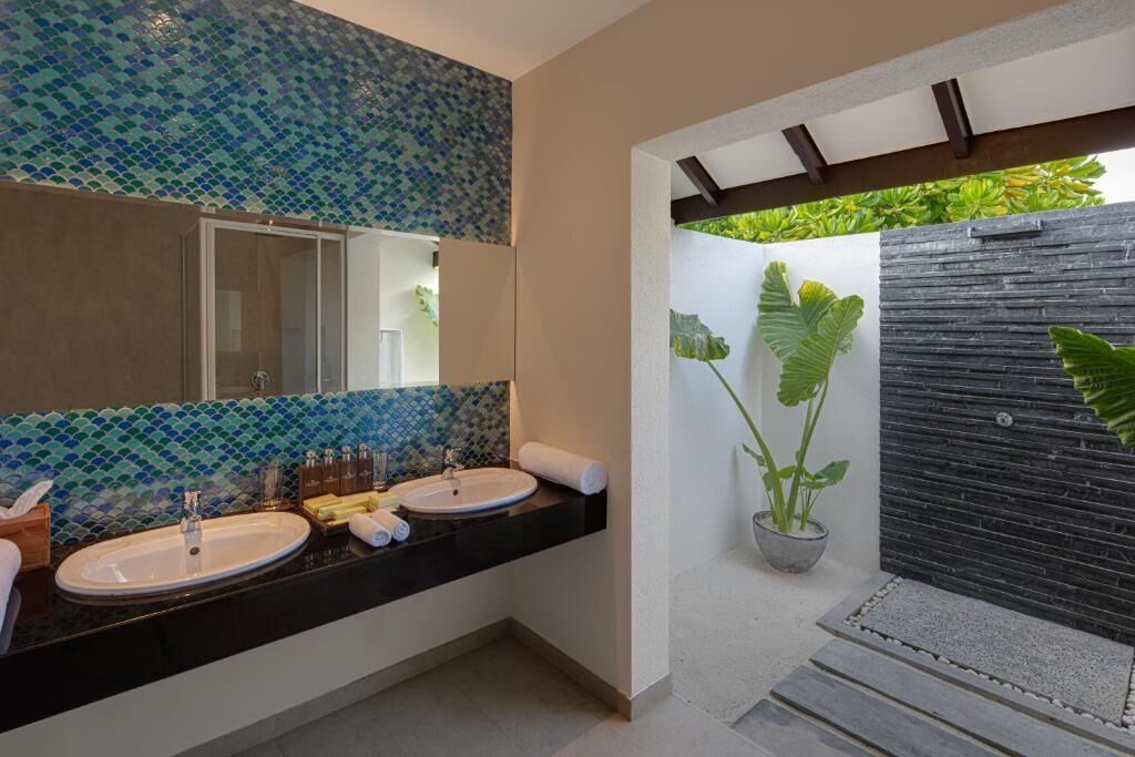 A modern bathroom with two sinks, a large mirror, and a potted plant.