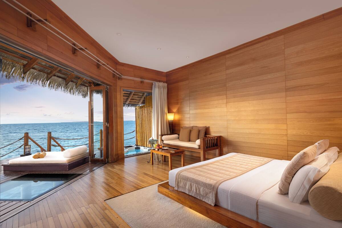 A bedroom with a bed, a sofa, a small table, and a view of the ocean.