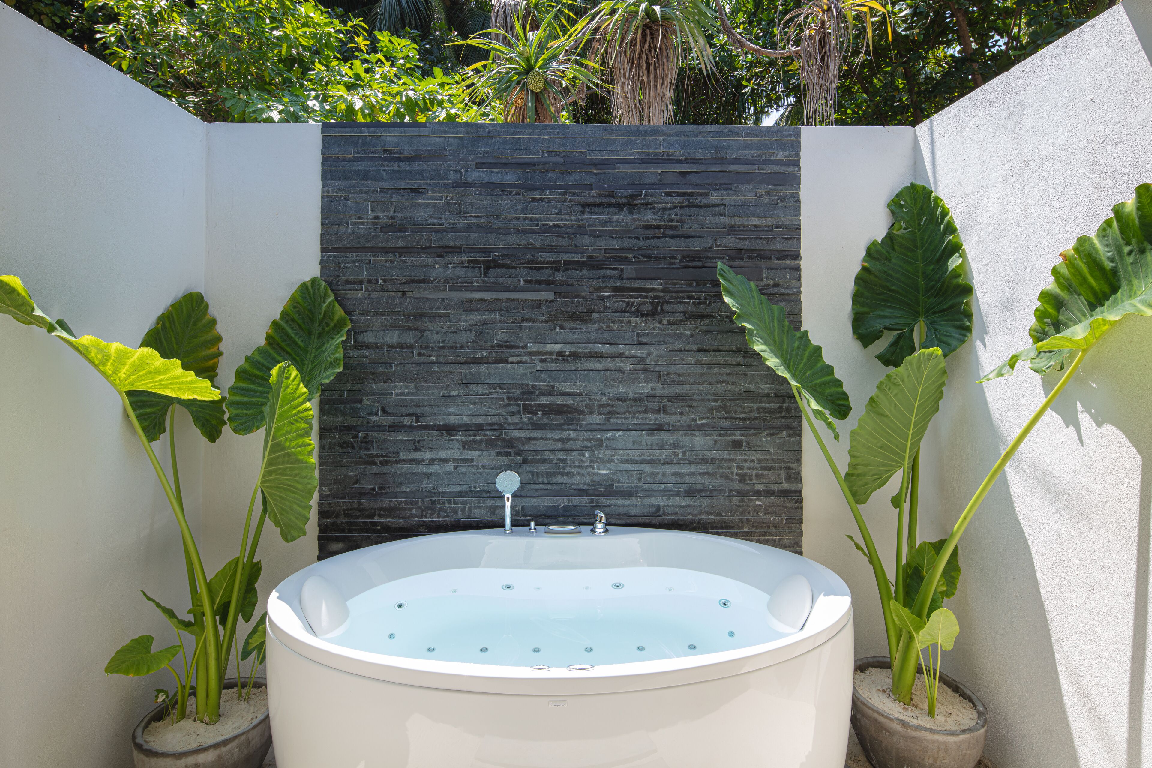 A spa area with a freestanding bathtub, a stone wall, and large tropical plants.