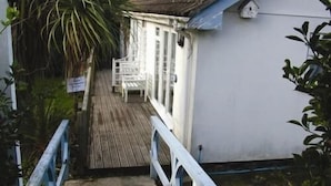 A wooden deck leading to a white building with a covered area. - The Driftwood Spars (St. Agnes)