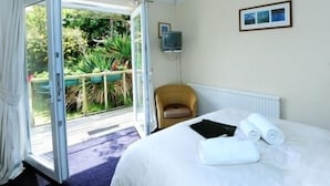 A hotel room with a bed, a chair, a TV, and a view of greenery outside. - The Driftwood Spars (St. Agnes)