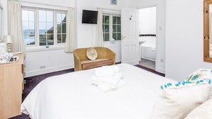A hotel room with a large bed, a wooden chair, a television, and a view of the sea through the windows. - The Driftwood Spars (St. Agnes)