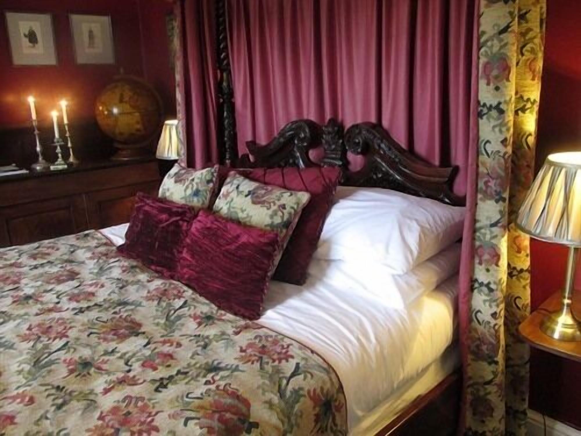 Una cama con ropa de cama floral, un cabecero con un reloj y una lámpara de noche.