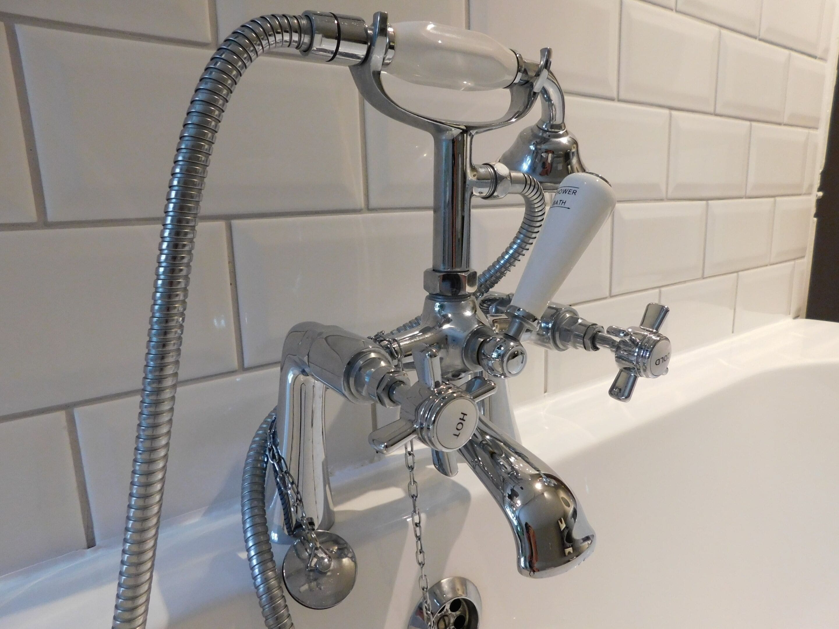 A bathroom with a chrome shower head, multiple faucets, and a flexible hose.