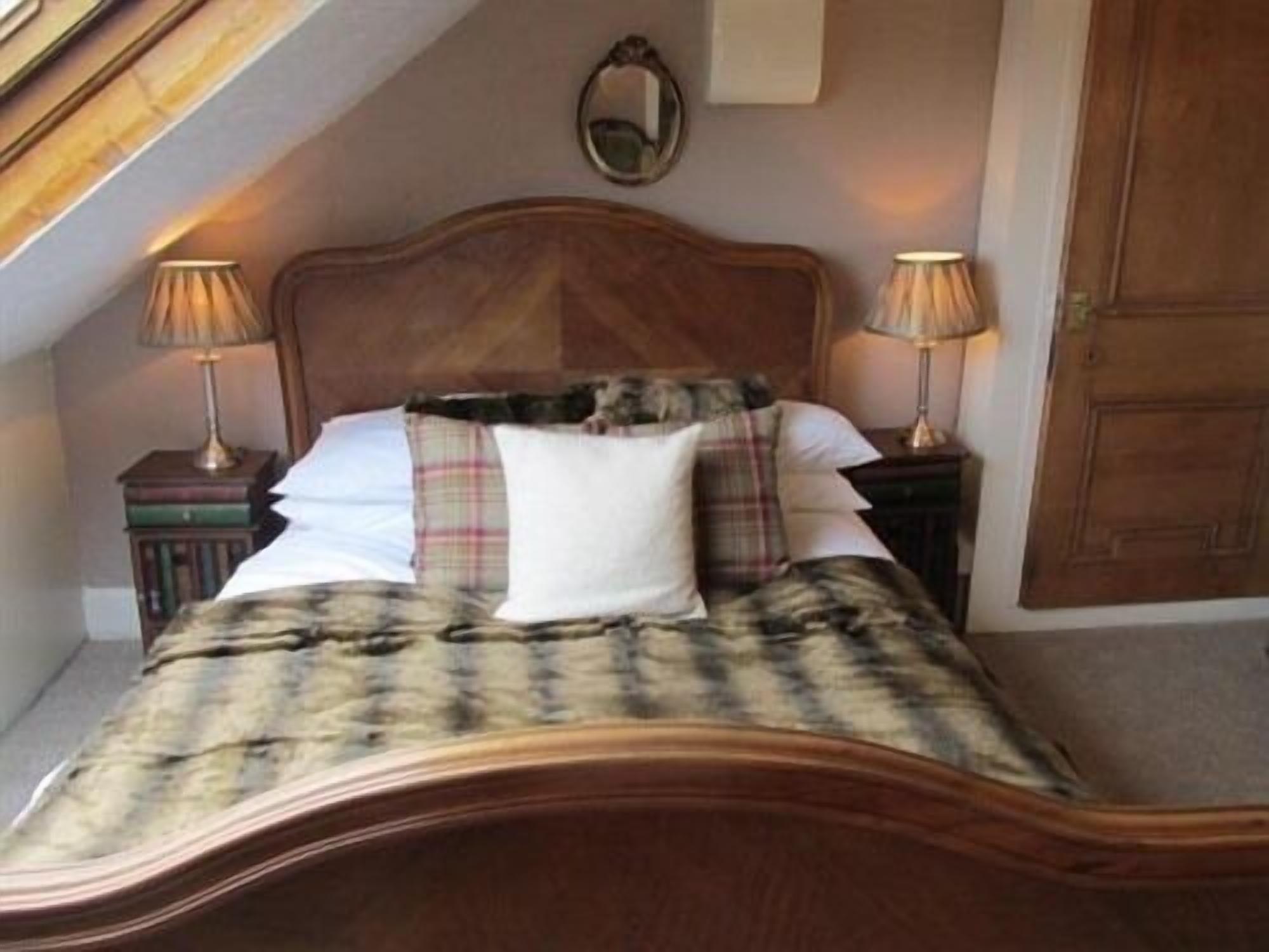 A bedroom with a wooden bed, two bedside lamps, a mirror on the wall, and a door.