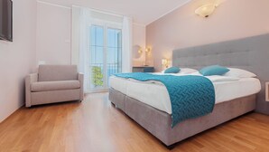 Ein Schlafzimmer mit Bett, Sessel, Schreibtisch und Balkon.