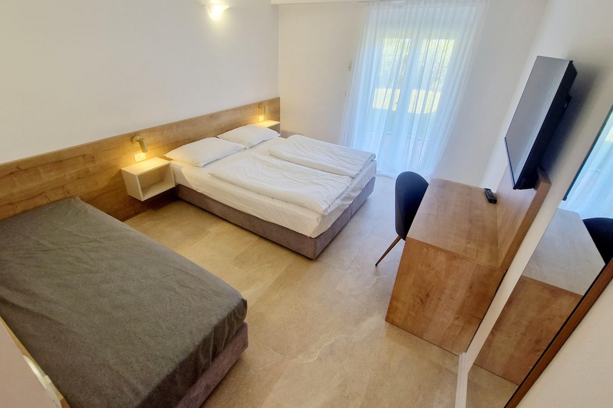 Ein Hotelzimmer mit Bett, Nachttisch, Stuhl, Schreibtisch und Fernseher.