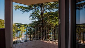 Ein Balkon mit Fliesenboden und Metallgeländer, mit Blick auf ein Gewässer und Bäume.