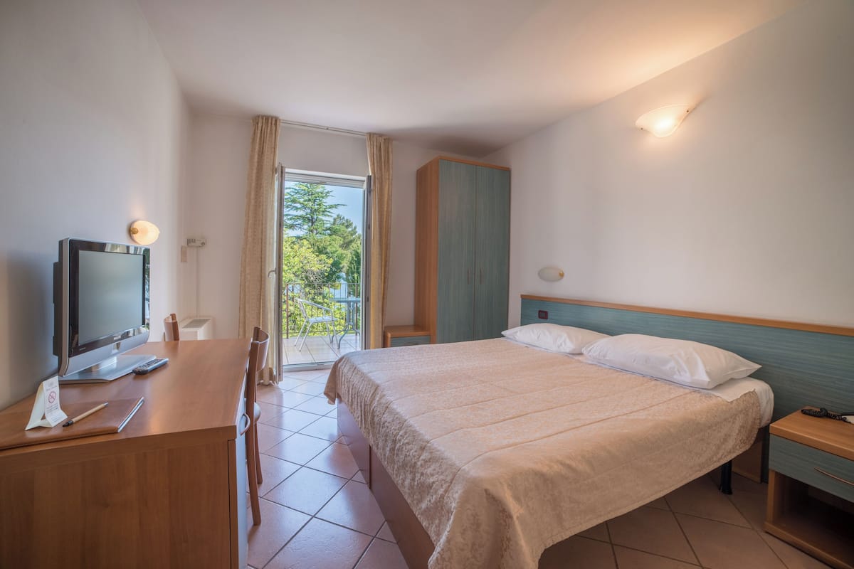 Ein Hotelzimmer mit Bett, Schreibtisch, Computer, Fernseher und Blick ins Freie.