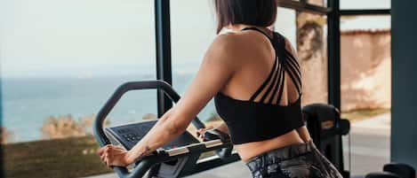 A person using a stationary bike with a view of the outdoors through large windows.