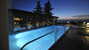 Una piscina interior con paredes de vidrio, solárium con baldosas y mobiliario exterior.