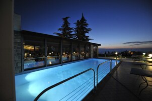 Una piscina interior con paredes de vidrio, solárium con baldosas y mobiliario exterior.