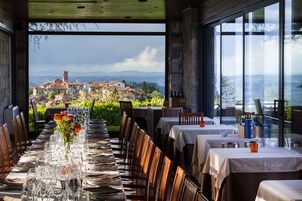 Un restaurante con una larga mesa preparada para comer, un jarrón con flores y vistas a un pueblo y montañas al fondo.