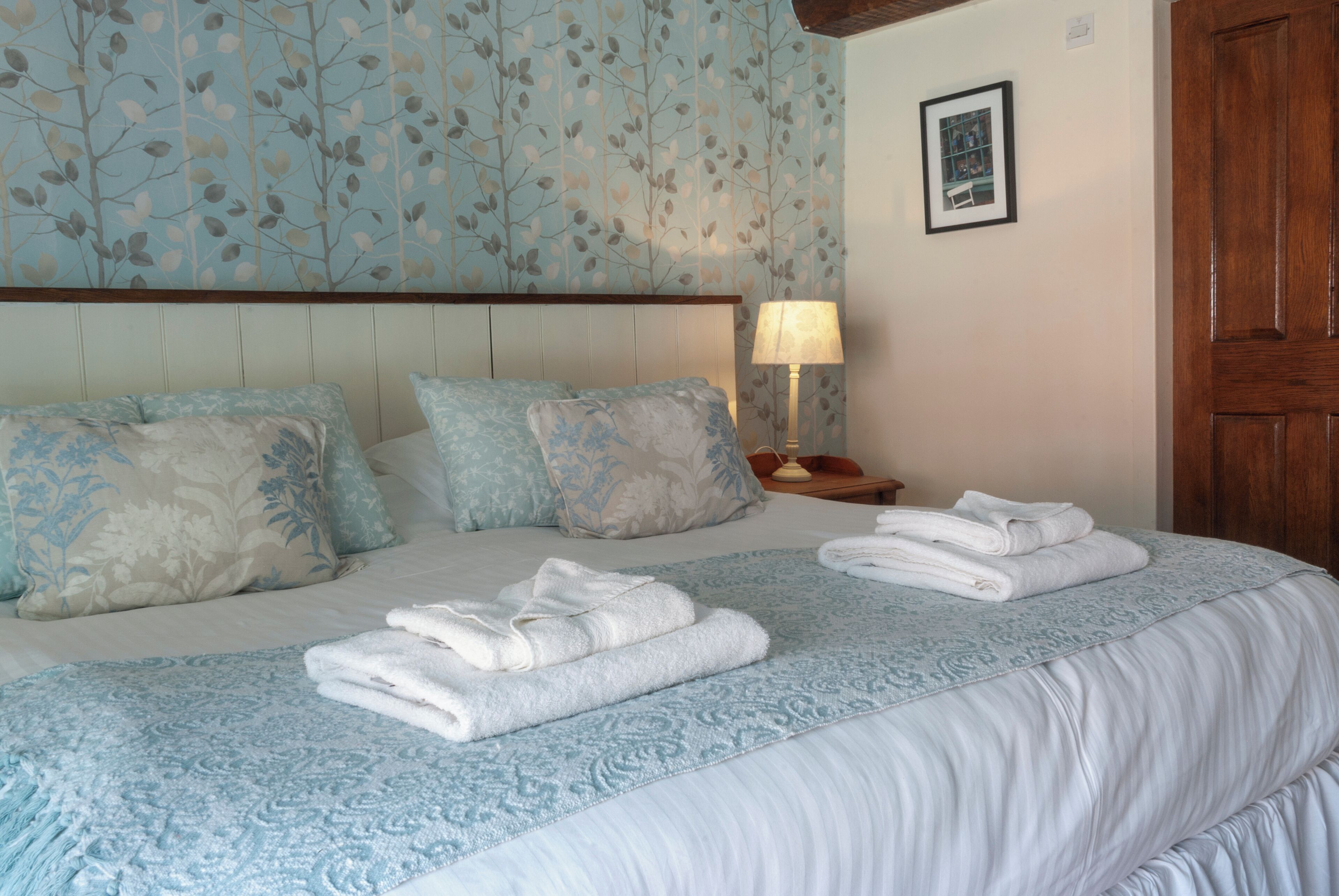 A neatly made bed with folded towels, a headboard, and a wall with a leaf pattern.