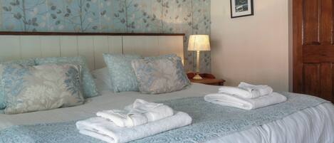 A neatly made bed with folded towels, a headboard, and a wall with a leaf pattern.