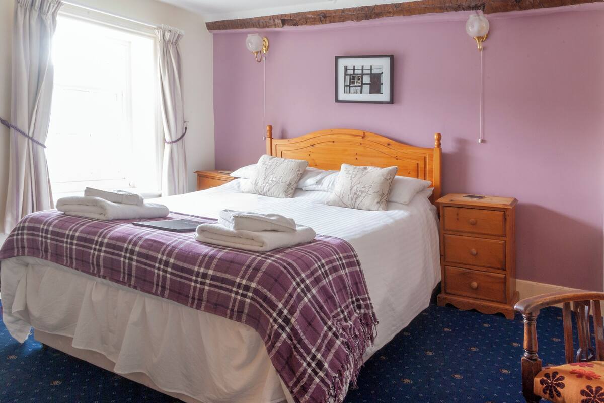 A neatly made bed with a purple and white checkered blanket, a wooden headboard, and two bedside tables with drawers.