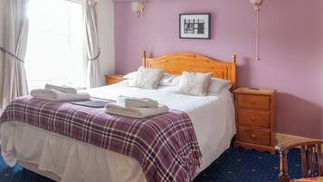 A neatly made bed with a purple and white checkered blanket, a wooden headboard, and two bedside tables with drawers.