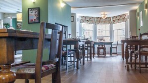 A dining area with wooden furniture, a large window with floral curtains, and a chandelier. - The Dragon Hotel (Montgomery)