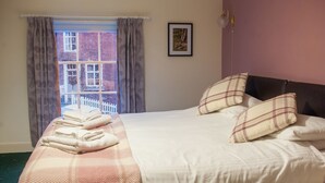 A neatly made bed with a pink and white checkered blanket, two pillows, and a set of folded towels. - The Dragon Hotel (Montgomery)