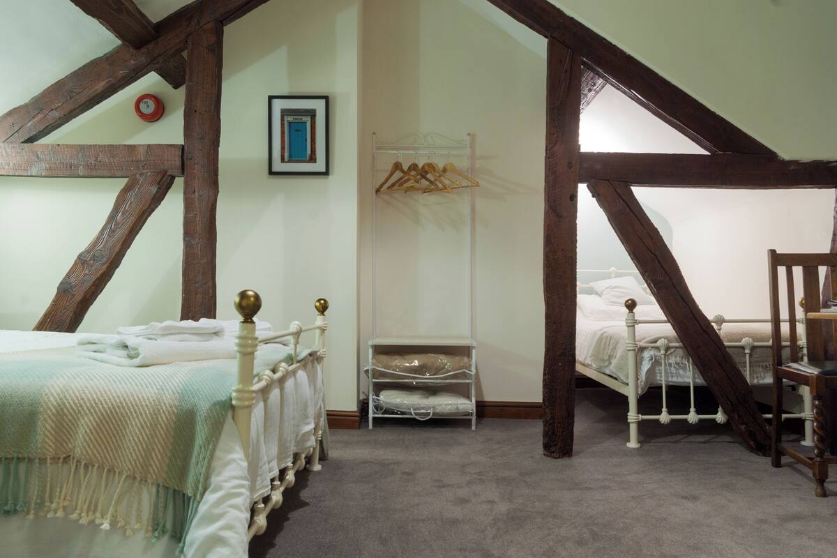 A bedroom with two beds, wooden beams, a coat rack, and a framed picture on the wall.