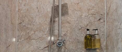 A shower with a handheld showerhead and a wall-mounted faucet, set against a marble wall.