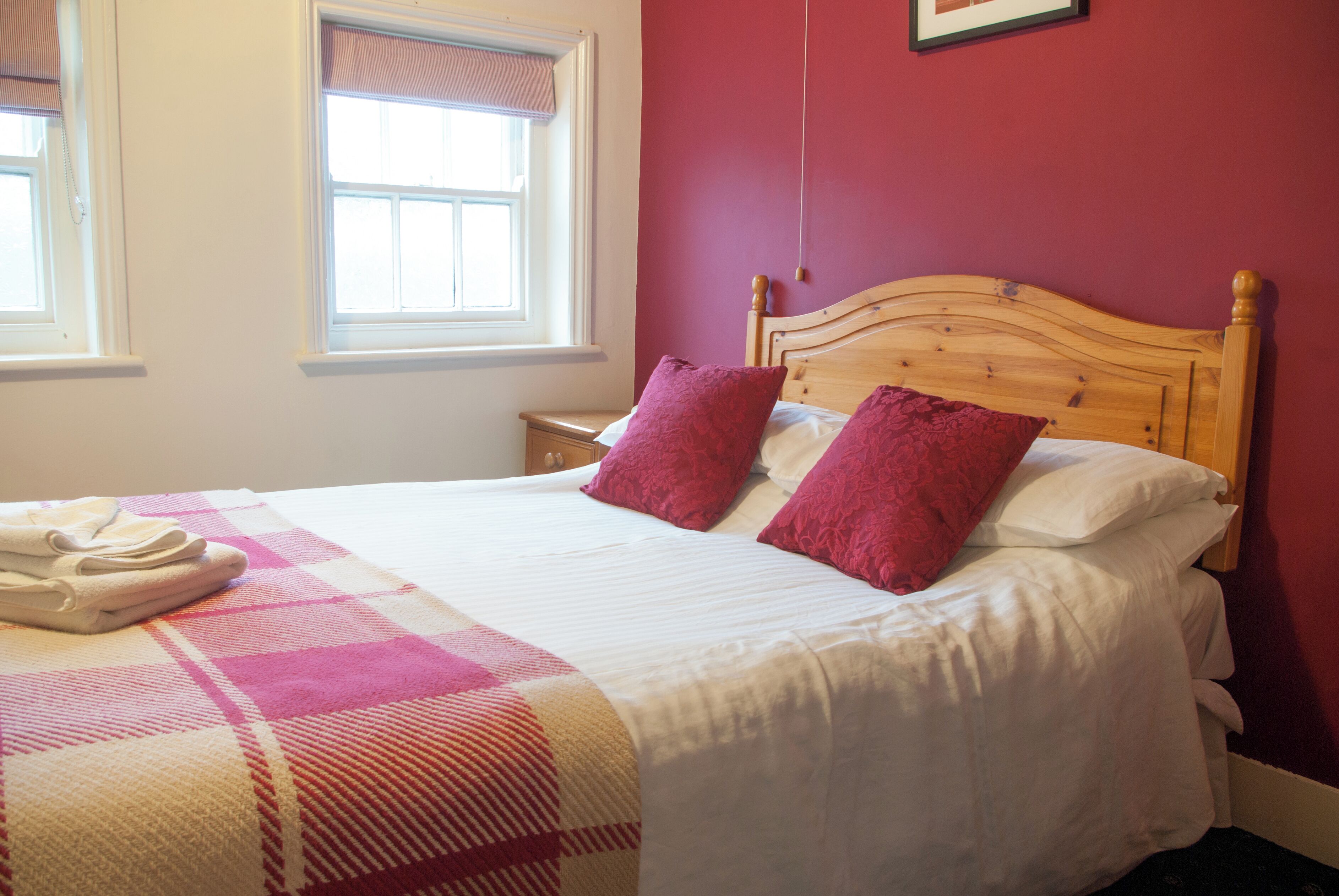 A neatly made bed with a checkered blanket, two pillows, and a folded towel on the side.