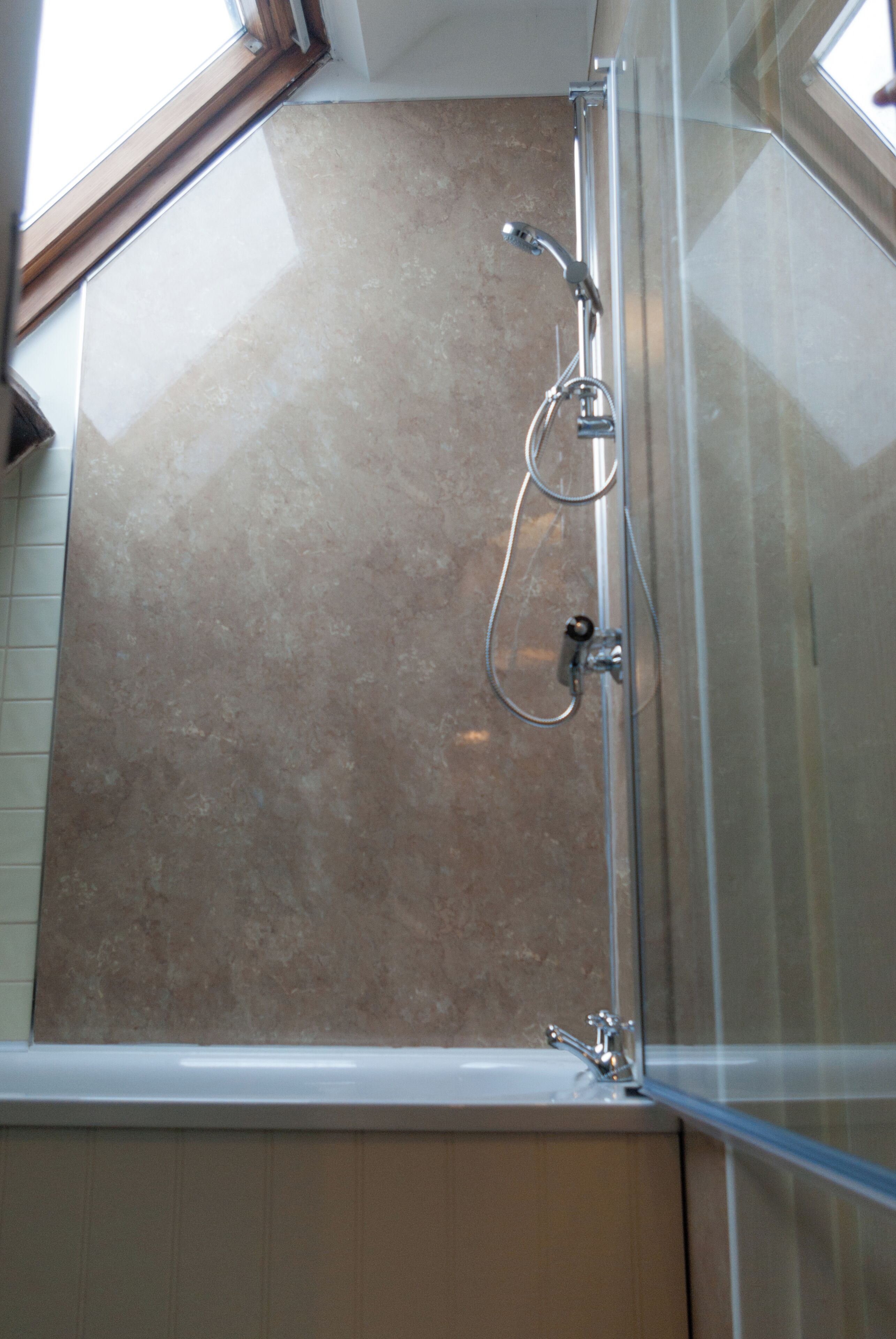 A bathroom with a glass shower enclosure, a visible showerhead, and a tiled wall.