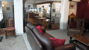 A spacious living area with a leather sofa, a wooden coffee table, and a red throw pillow. A wooden chair and a dining table with chairs are visible in the background. - The Dragon Hotel (Montgomery)