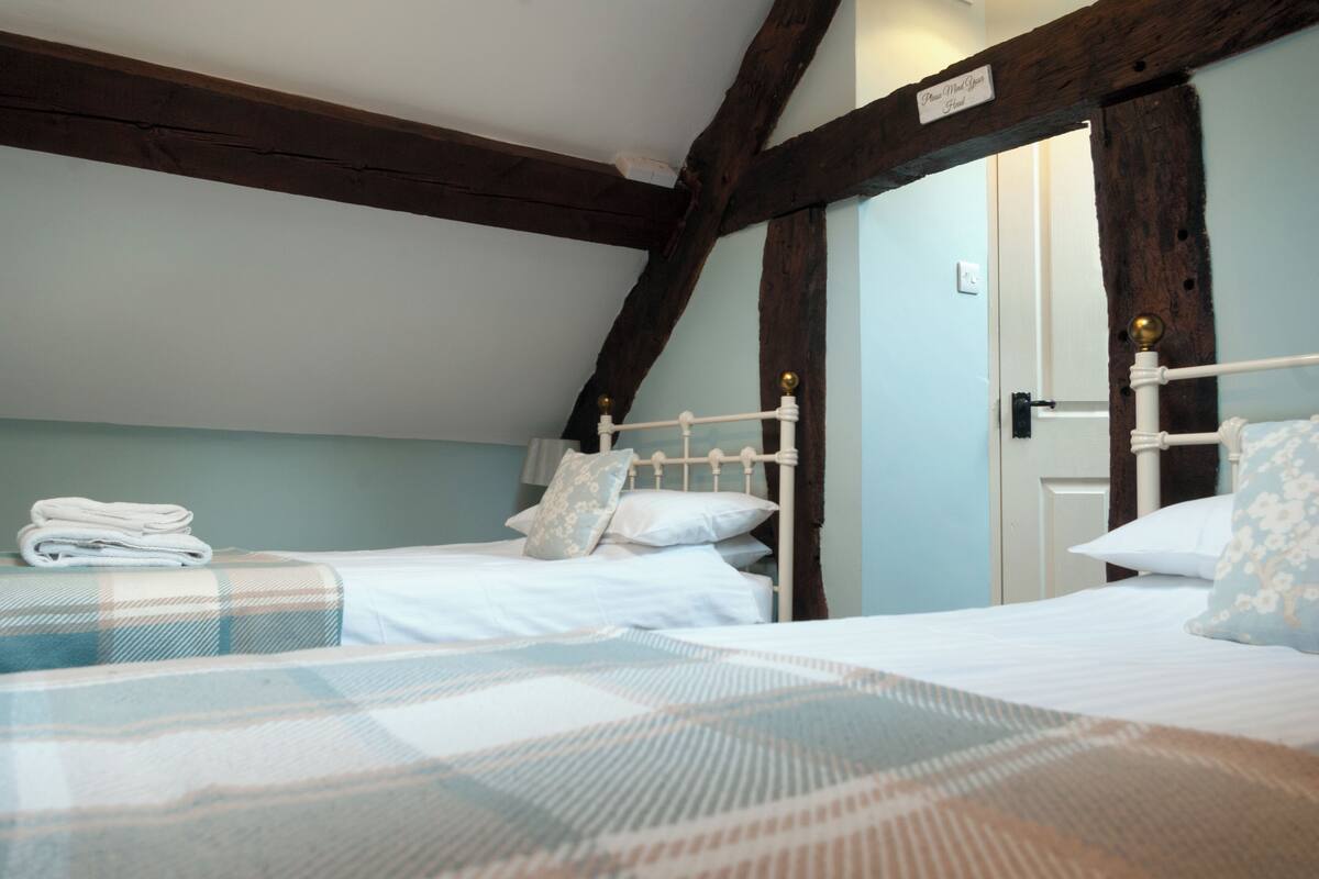 A bedroom with two single beds, a wooden ceiling, and a door with a sign.