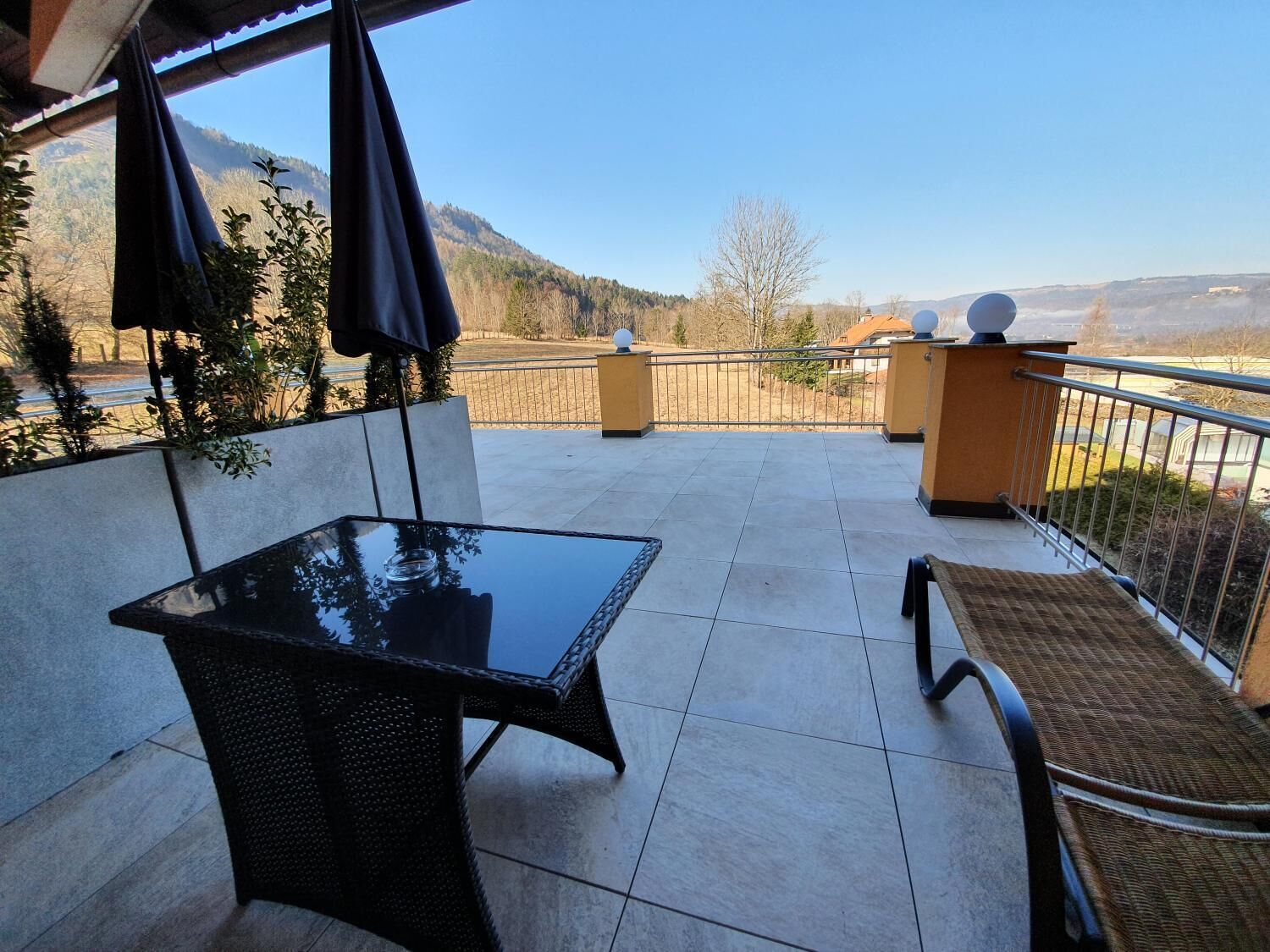 A balcony with a glass table, wicker chairs, and a view of a mountainous landscape.