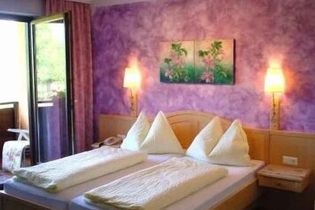A hotel room with a bed, two bedside lamps, a nightstand, and a window with curtains.