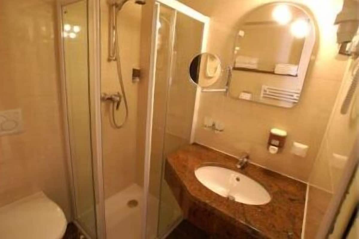 A bathroom with a glass-enclosed shower, a sink with a marble countertop, and a mirror with a light above it.