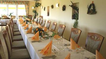 A long dining table set with chairs, each with a napkin holder, in a well-lit room with decorative wall hangings.