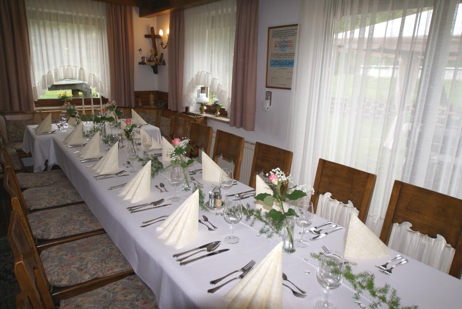 A long dining table set for a formal event with white tablecloths, silverware, and floral centerpieces.