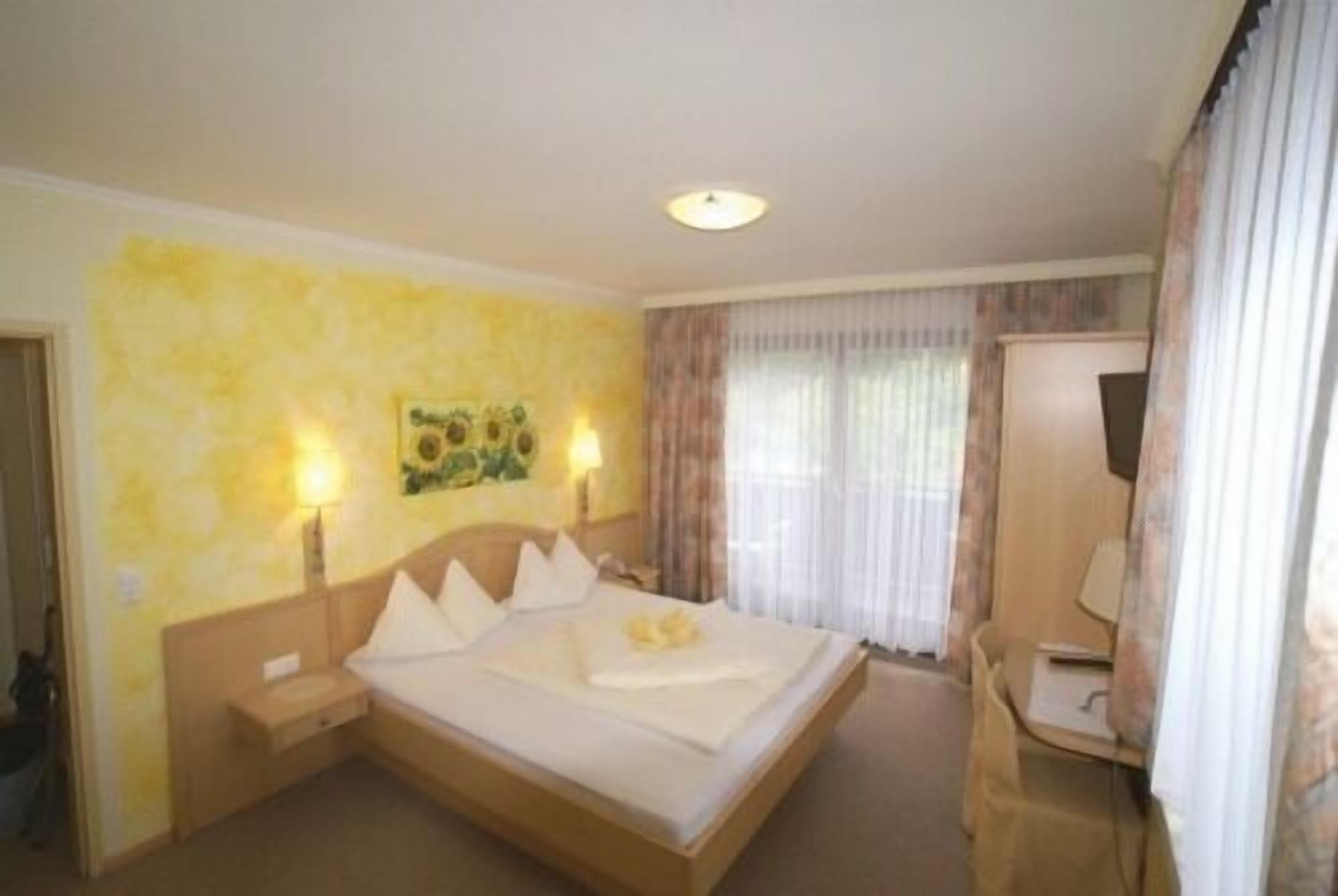 Quarto de hotel com uma cama grande, abajures, um quadro na parede e uma janela com cortinas.