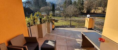 A balcony with wicker furniture, a view of mountains, and a railing.