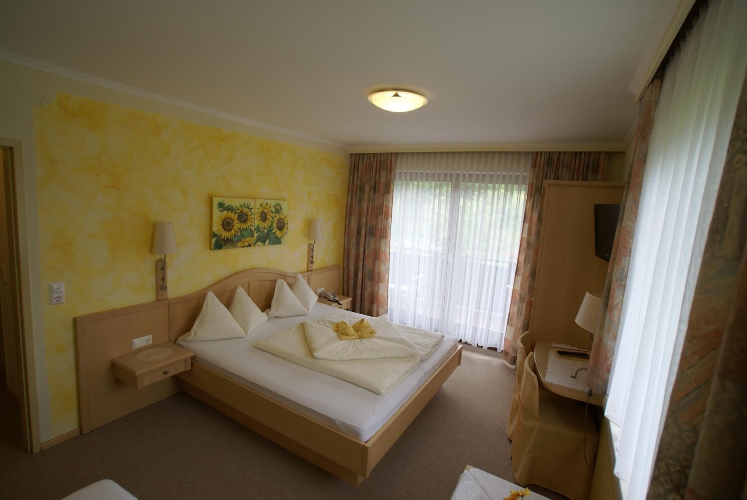 Ett hotellrum med en stor säng, ett nattduksbord, en lampa, en tavla och ett fönster med gardiner.