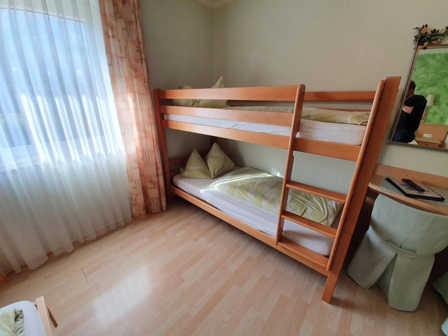 Una cama litera con tres niveles, un escritorio de madera, una silla y un espejo en la pared.