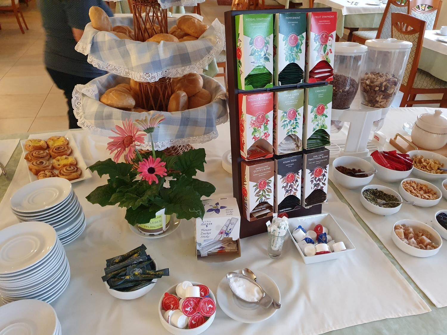 Una mesa de buffet con diversos alimentos, incluyendo pasteles, salsas y aderezos, decorada con un centro de flores.