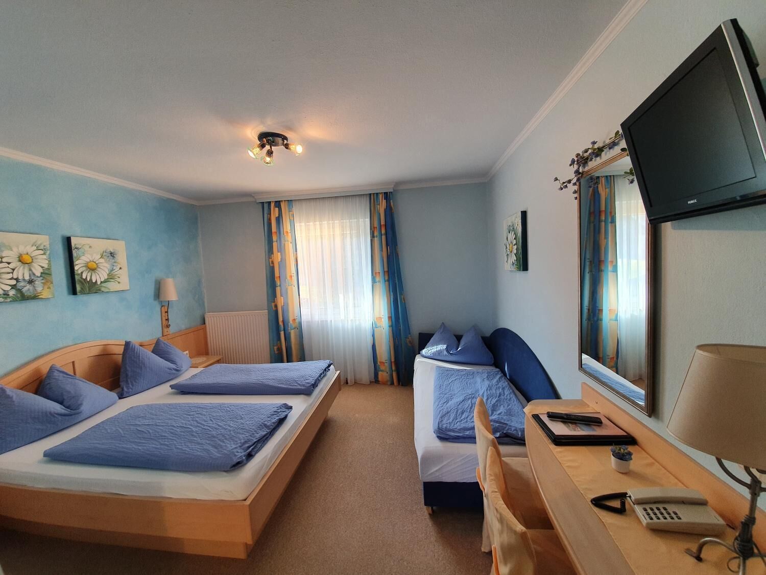 A hotel room with two beds, a desk, a chair, a TV, and a window with curtains.