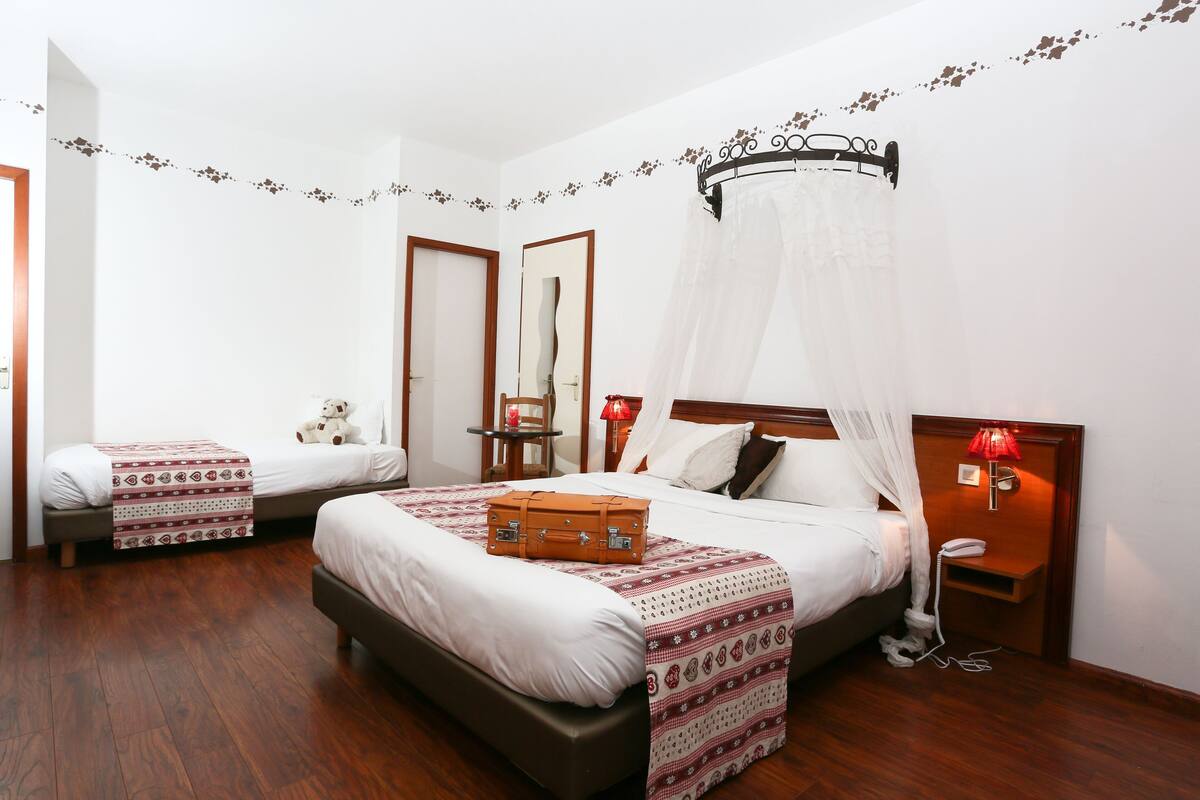 A hotel room with a large bed, a smaller bed, a nightstand with a lamp, a suitcase on the bed, and a mirror on the wall.