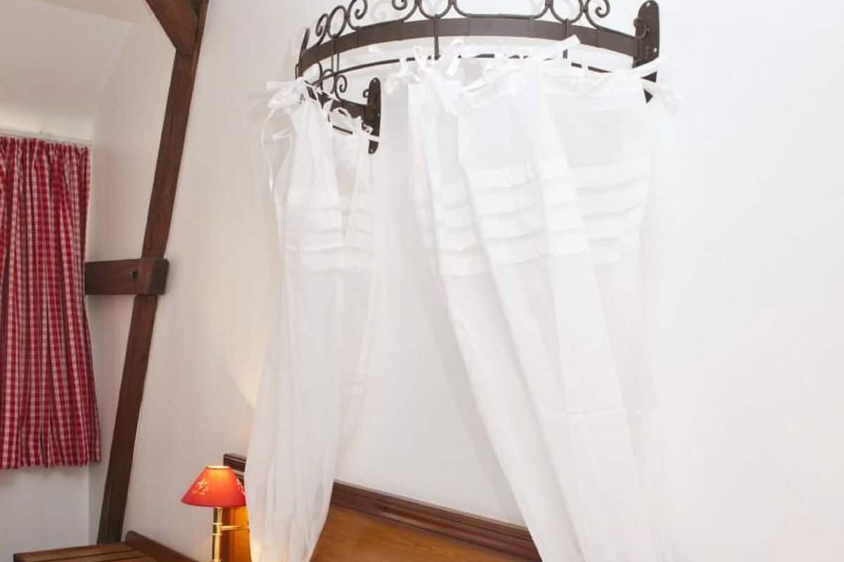 A bed with white linens, a red and white checkered skirt, a wooden headboard, and two bedside lamps.