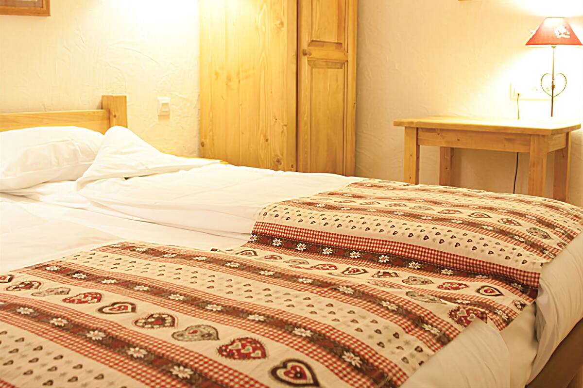 A bedroom with a wooden wardrobe, a bedside table, and a bed with a patterned bedspread.