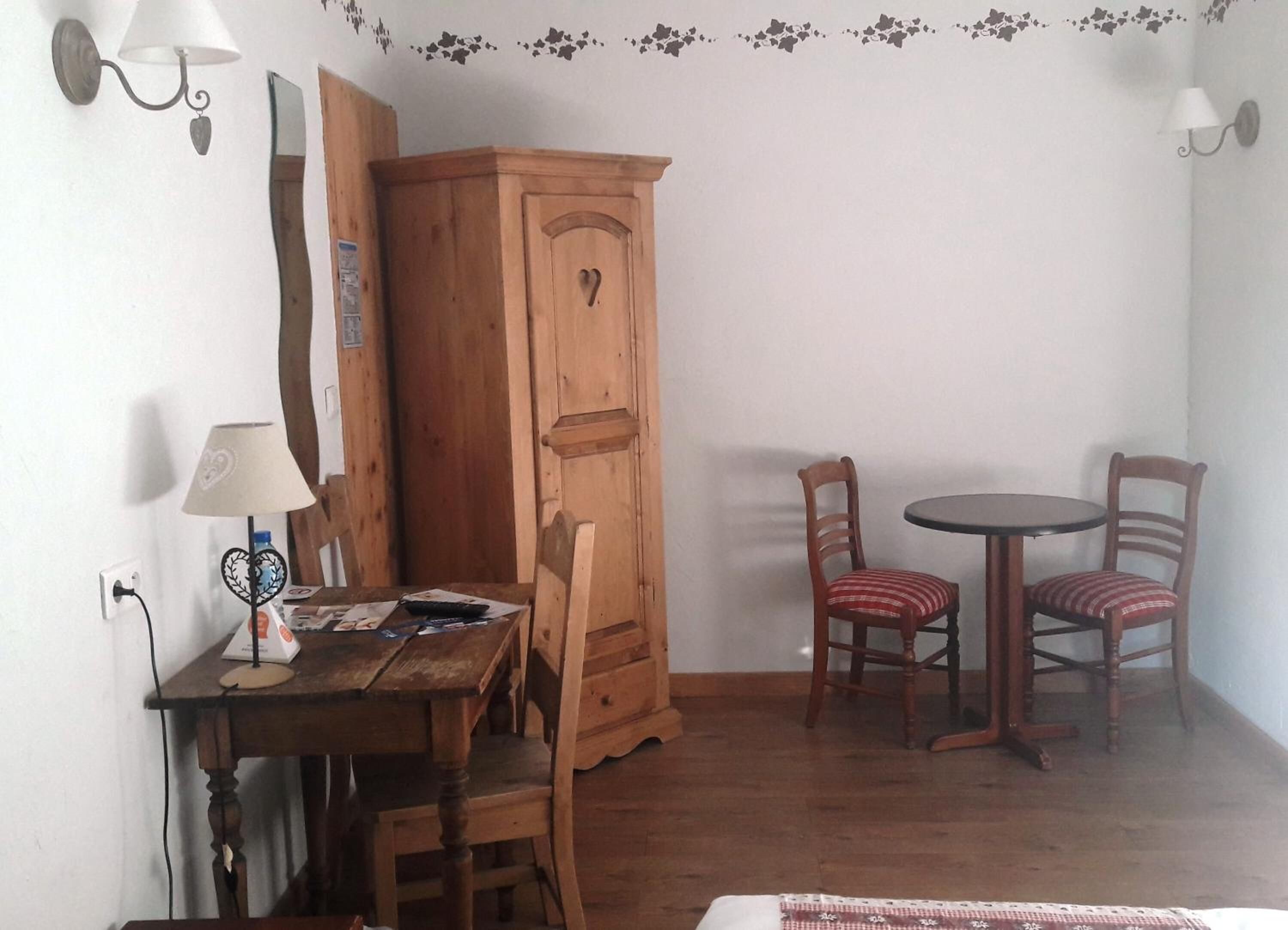 Une pièce comprenant un meuble en bois, une table avec des chaises et deux lampes fixées au mur.