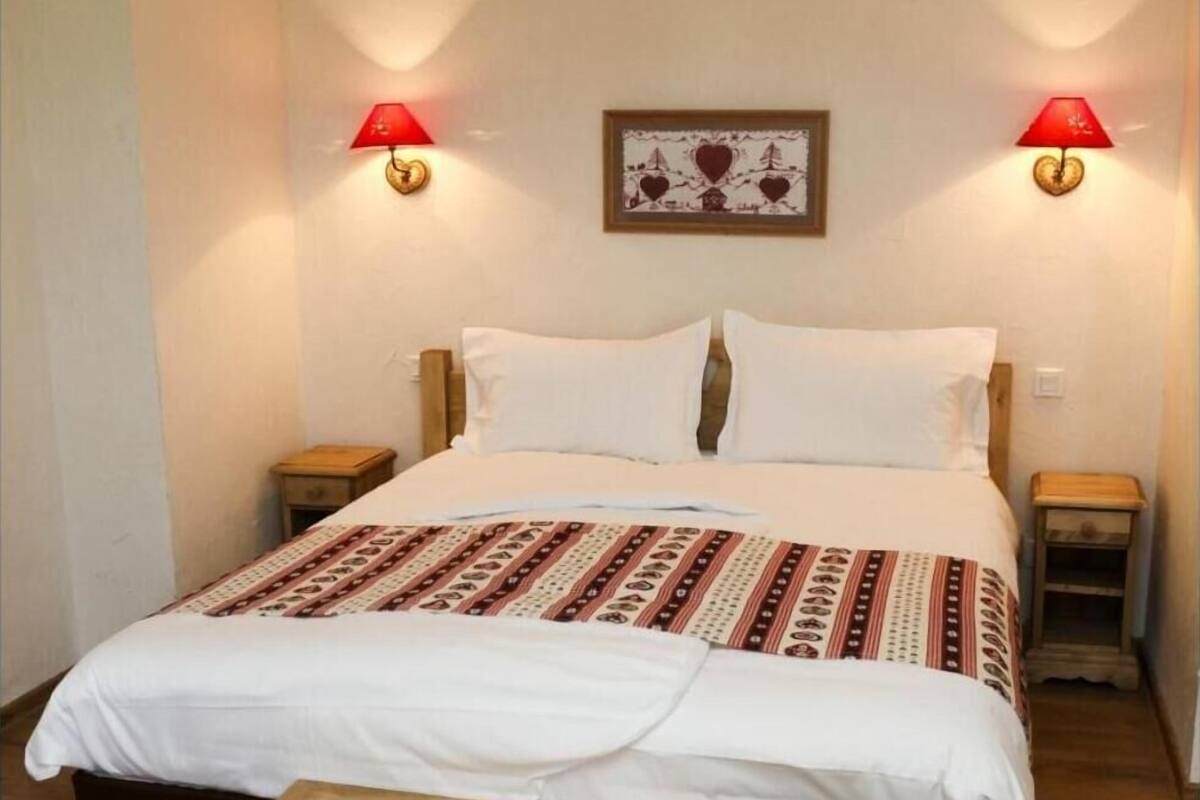 A bed with a patterned bedspread, two bedside tables with lamps, a wooden bench, and a wall-mounted picture.