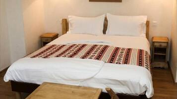 A bed with a patterned bedspread, two bedside tables with lamps, a wooden bench, and a wall-mounted picture.