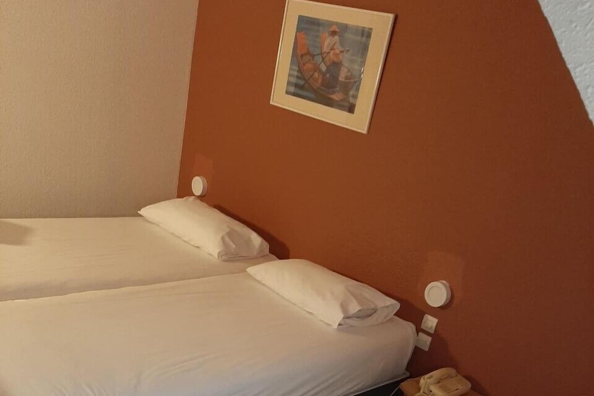 A hotel room with two single beds, a bedside table with a lamp, and a framed picture on the wall.