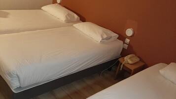 A hotel room with two single beds, a bedside table with a lamp, and a framed picture on the wall.