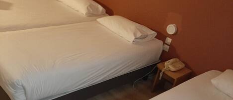 A hotel room with two single beds, a bedside table with a lamp, and a framed picture on the wall.